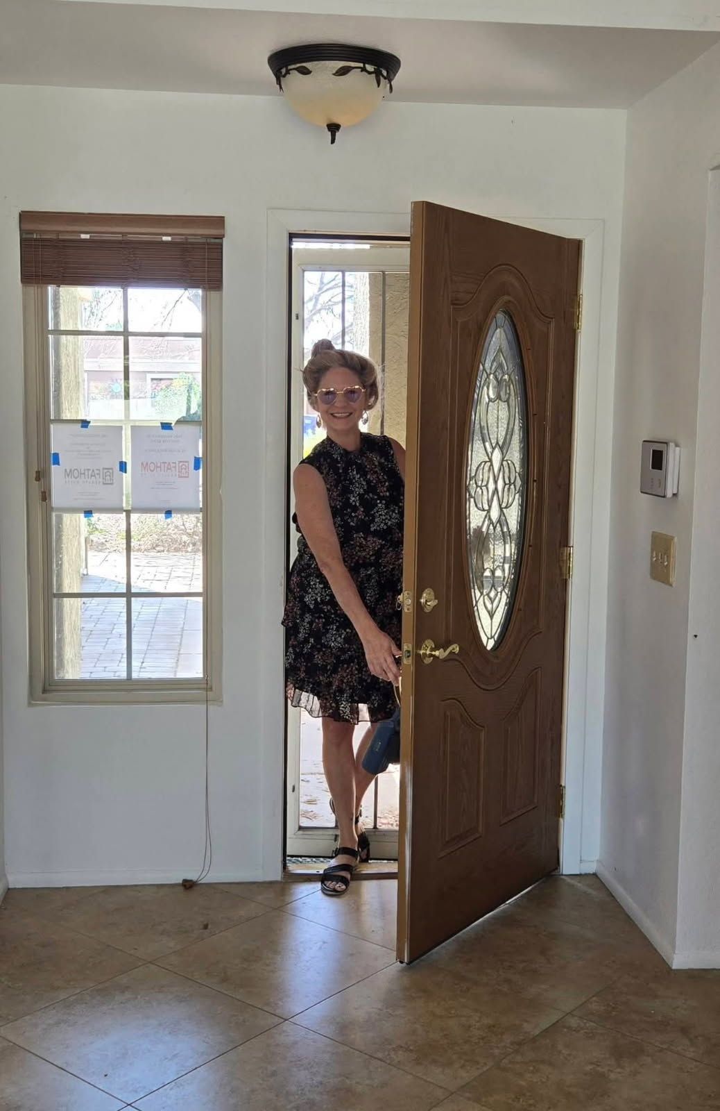 Person standing in a doorway of a bright entry hall, with a wooden front door open and a window beside it