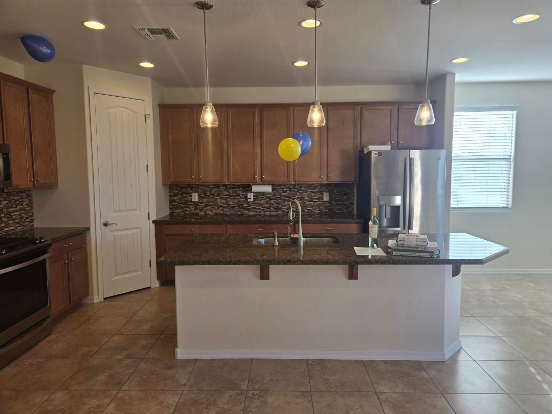 Modern kitchen with white island, wood cabinets, granite counters, stainless fridge, and blue-yellow balloons