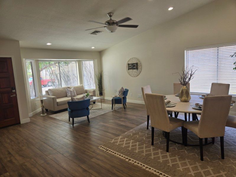 Spacious living and dining room with wood floors, beige chairs, blue accent chairs, and a ceiling fan