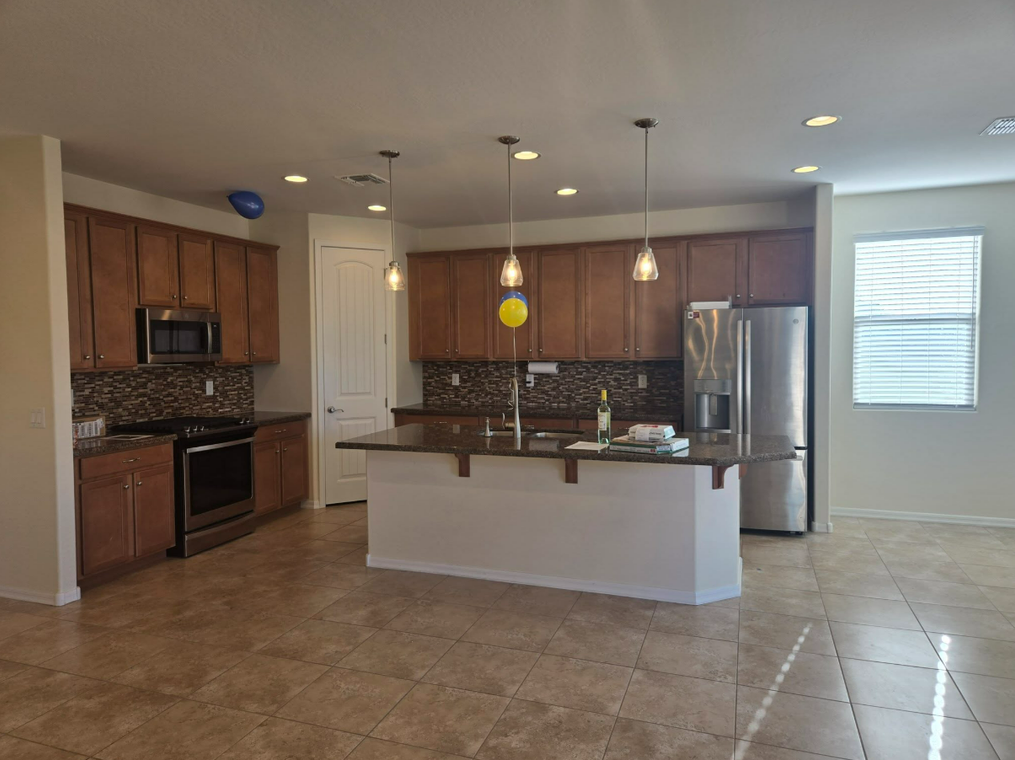 Open-plan kitchen with wood cabinets, granite island, stainless appliances, and tile flooring