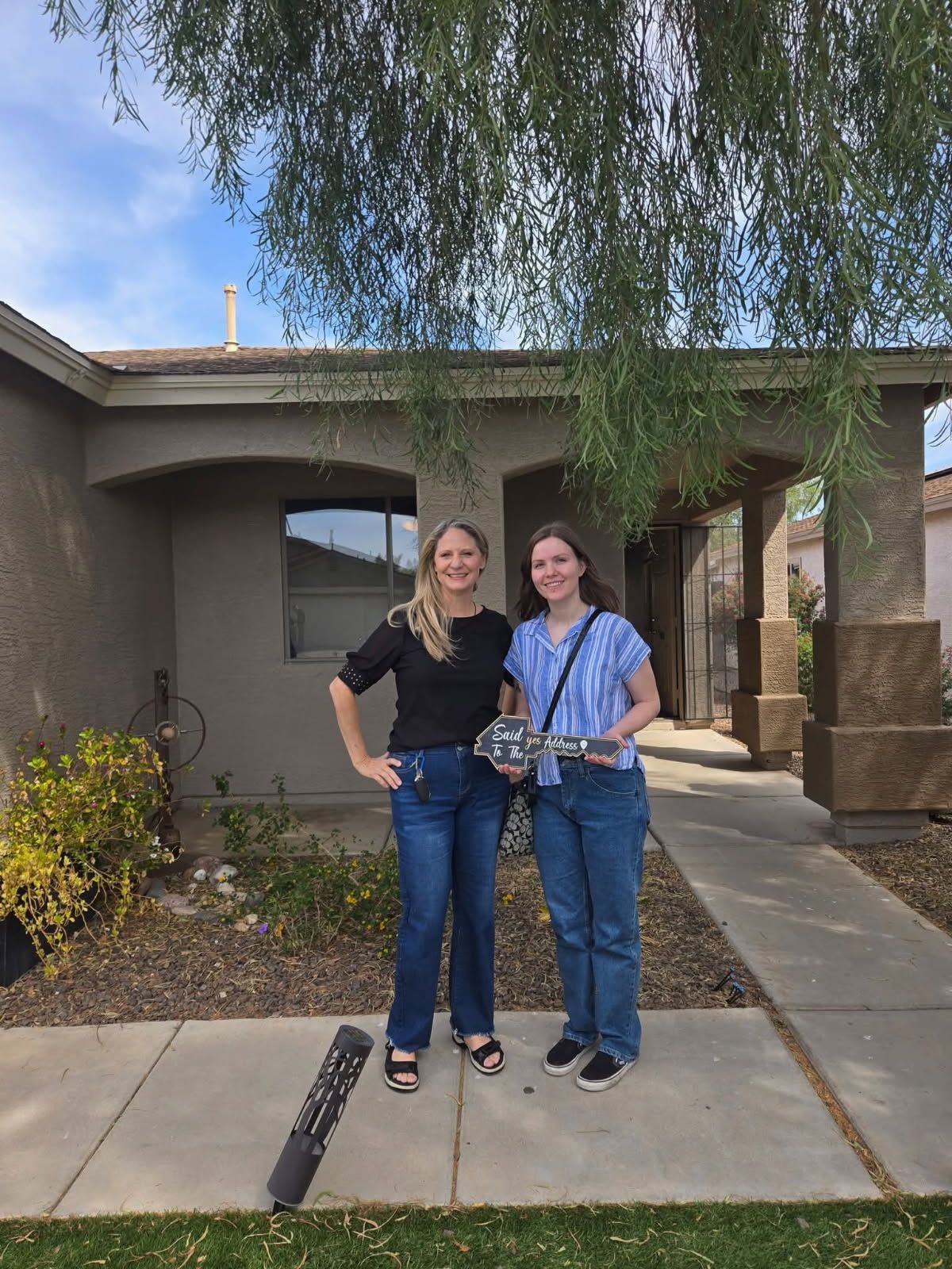 Two people standing on a sidewalk outside a house, smiling and holding a small drone camera.