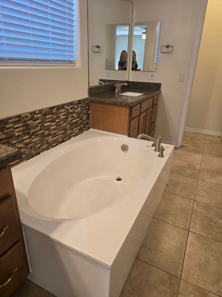 Bathroom with white soaking tub, brown vanity, mirror, and beige tile floor.