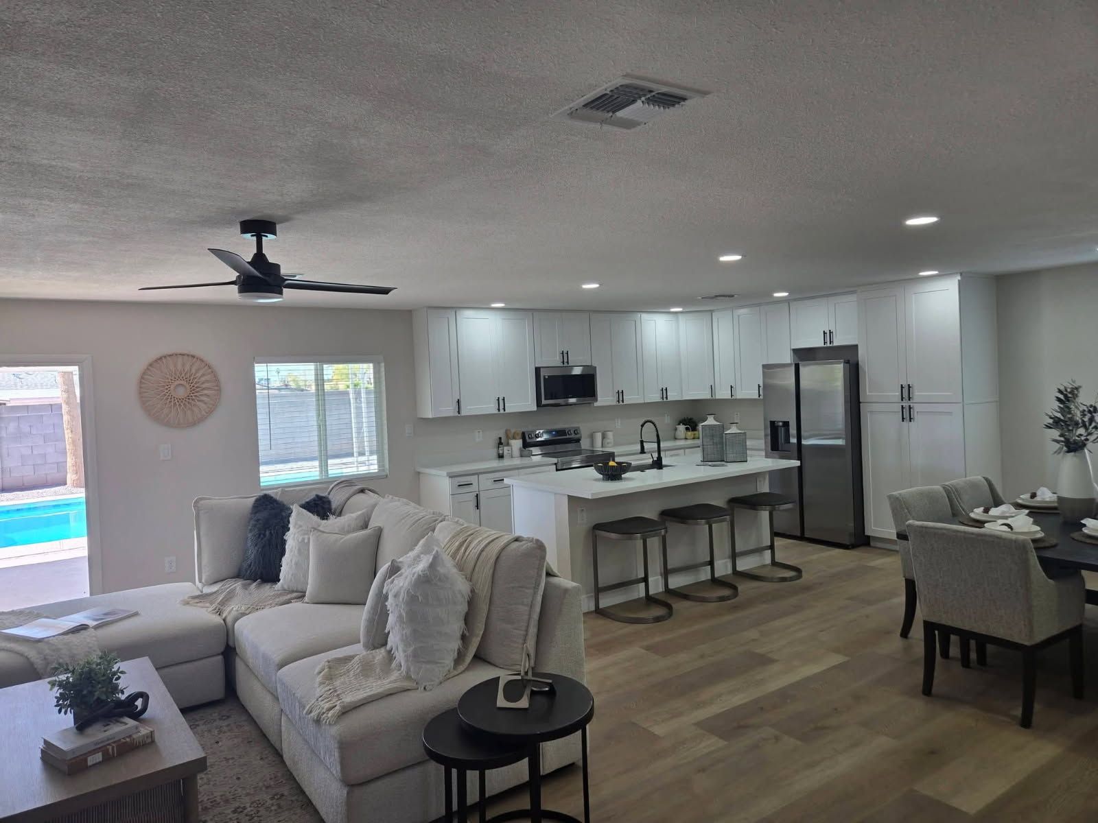 Bright open-concept living room and kitchen with white sofa, island, dining table, and wood floors