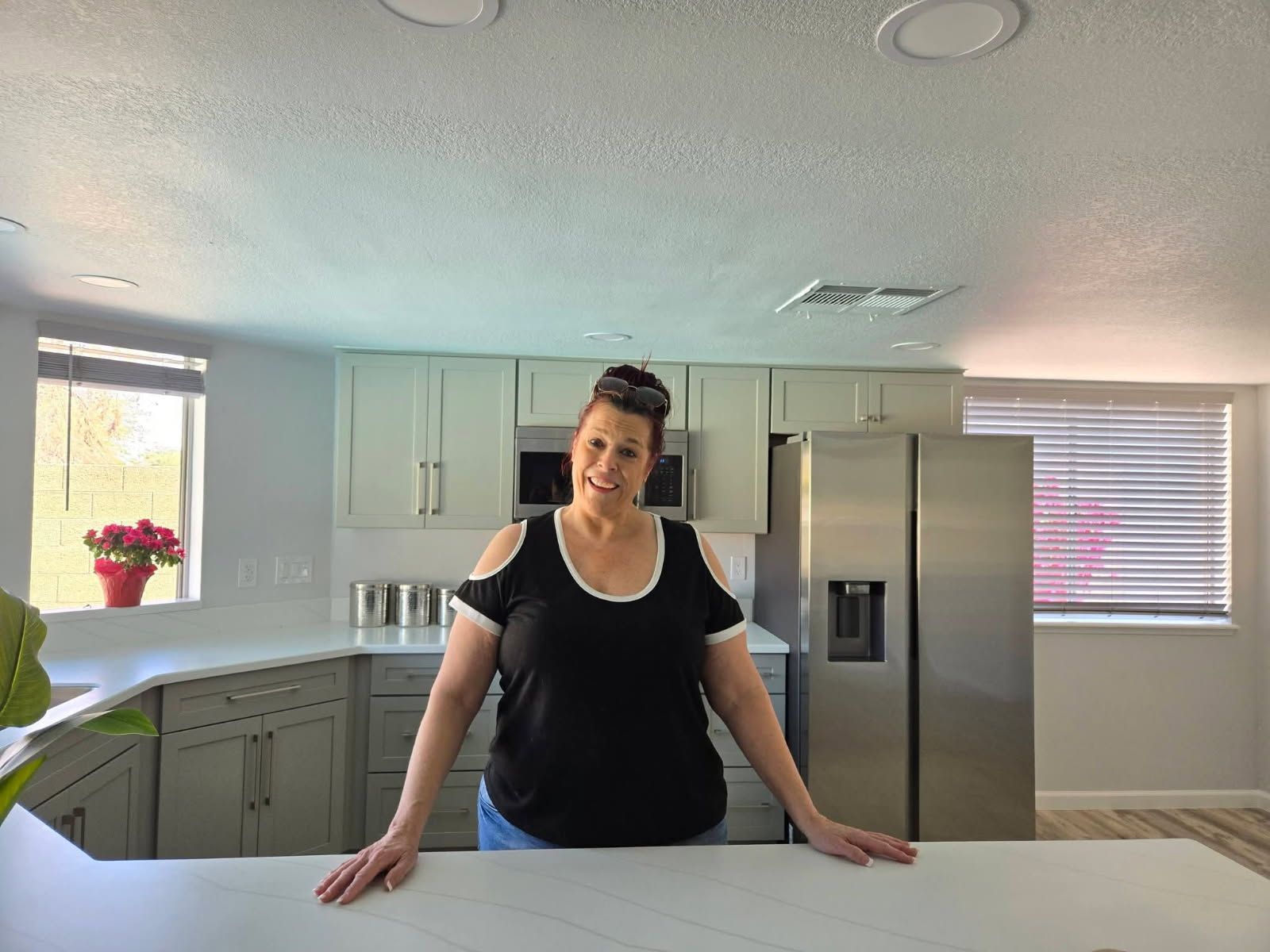Person leaning on a kitchen island in a bright, modern kitchen with stainless steel appliances.