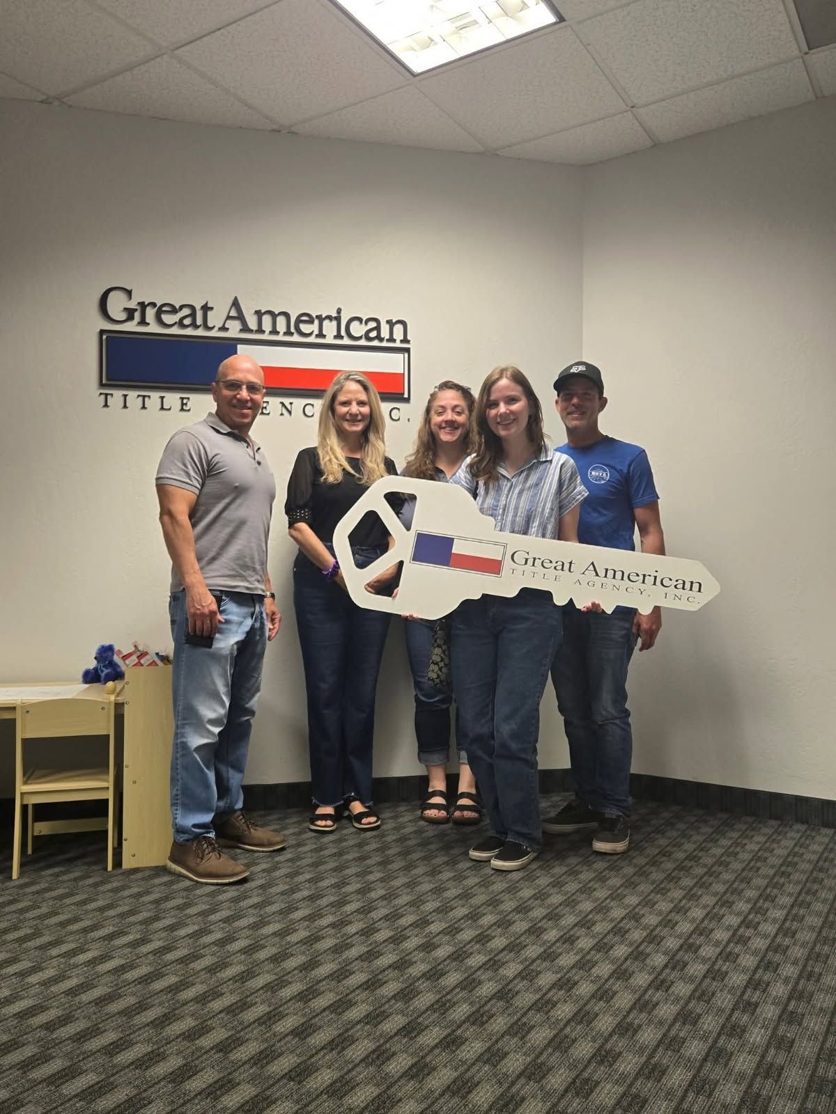Five people holding a large key in a Great American office lobby.