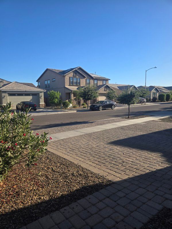 Suburban street with two-story houses, parked cars, and a clear blue sky, viewed from a driveway.