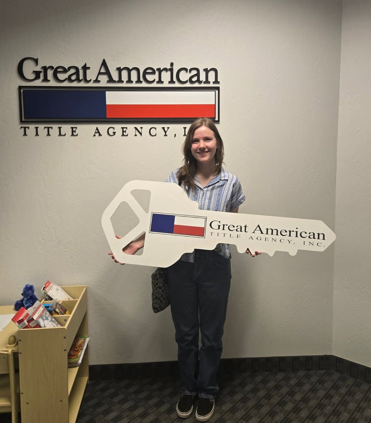 Person holding a large key-shaped sign in front of a Great American Title Agency wall logo.