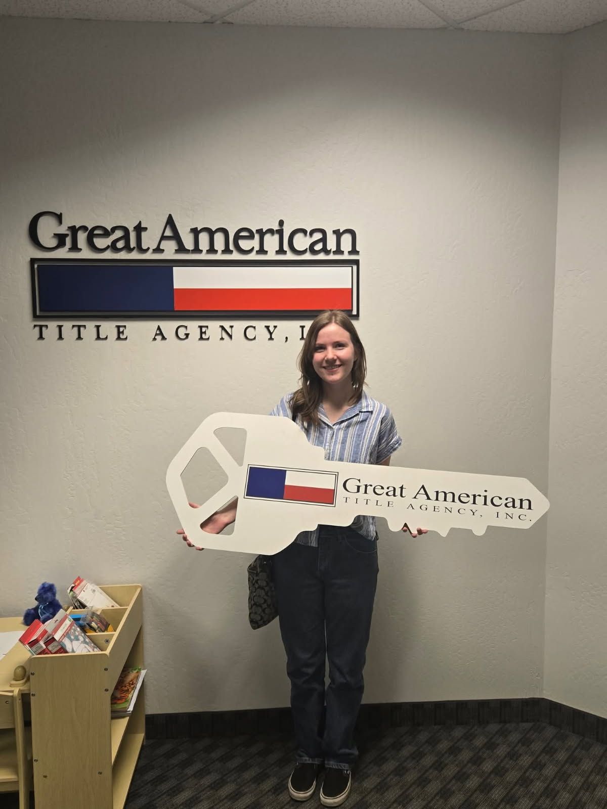 Woman holding a large key prop in front of a Great American Title Agency sign