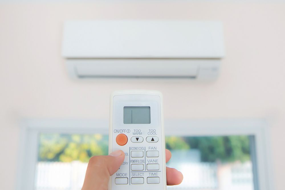A Person is Holding a Remote Control in Front of an Air Conditioner — Brite-Lec Pty Ltd in Currajong, QLD