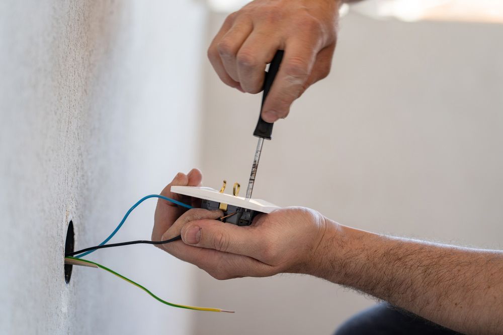 A man is fixing an electrical outlet with a screwdriver.