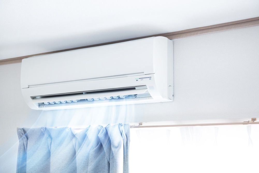 A White Air Conditioner is Hanging From the Ceiling in a Room Next to a Window — Brite-Lec Pty Ltd in Currajong, QLD