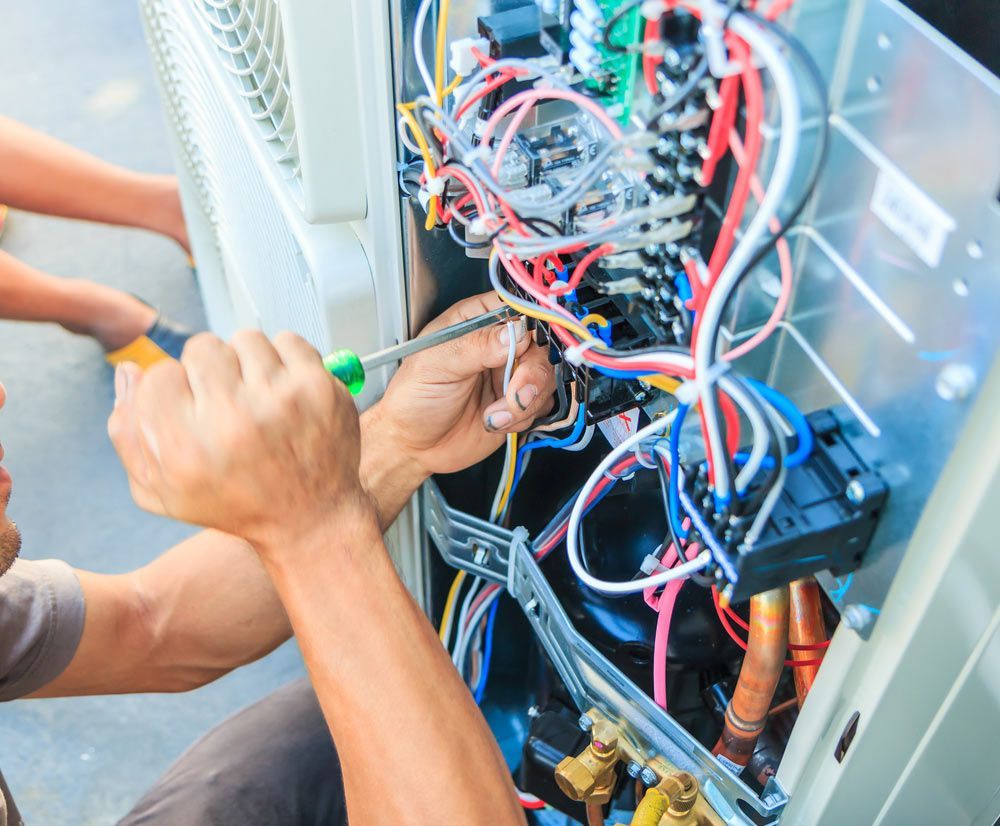 Two Men Are Working on an Air Conditioner With a Screwdriver and Wrench — Brite-Lec Pty Ltd in Currajong, QLD