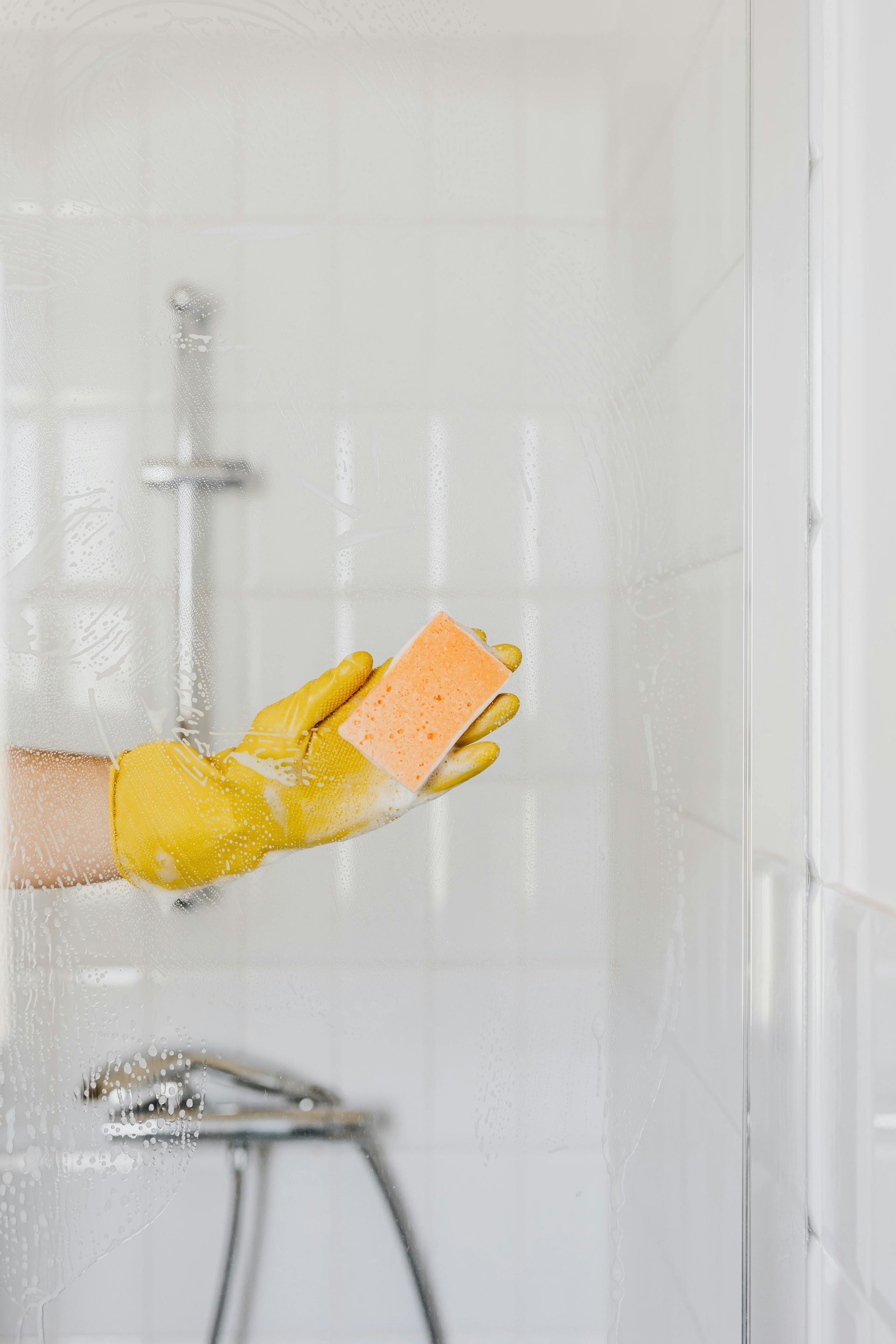 A person wearing yellow gloves is holding a sponge in a shower.