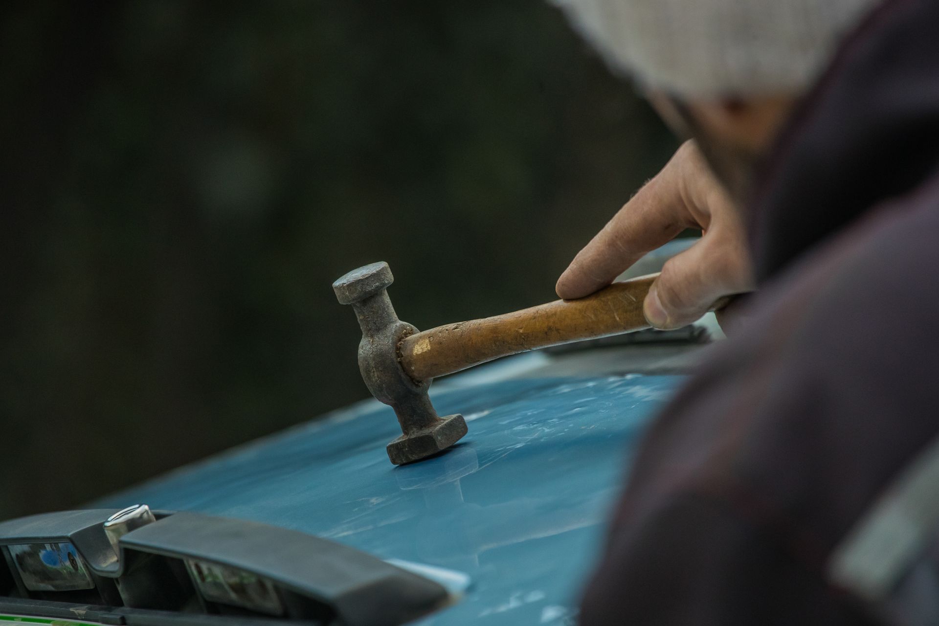 A partial view of an auto repair worker straightening dents with a special car panel hammer. A partial view of an auto repair worker straightening dents with a special car panel hammer.
