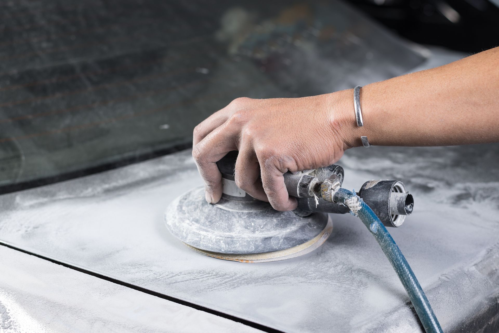 Hand using air sander to smooth a dusty car panel during repair work. Hand using air sander to smooth a dusty car panel during repair work.