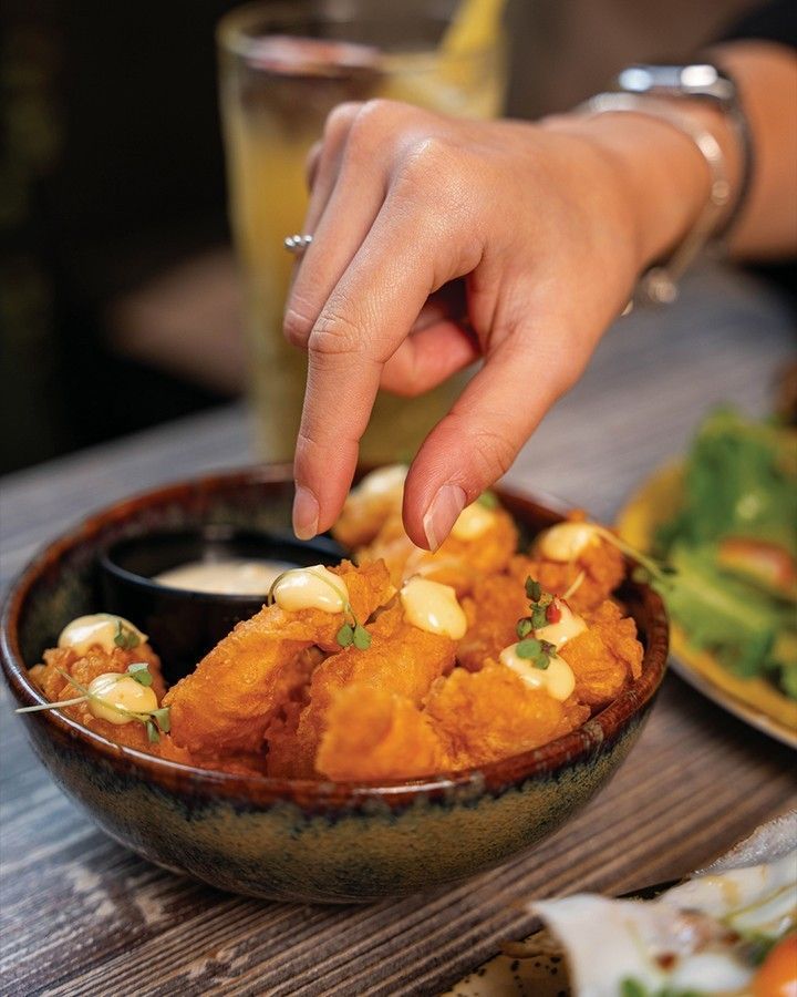 Uma pessoa está alcançando uma tigela de comida com o dedo, ideal para partilhar entre amigos
