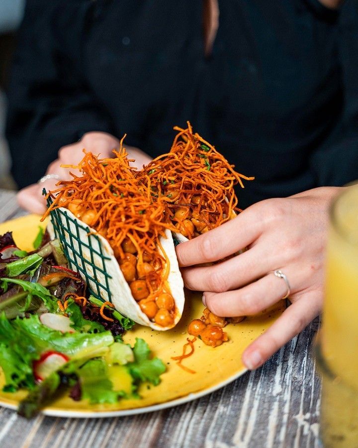Uma pessoa está comendo um taco com grão de bico e cenoura em um prato.