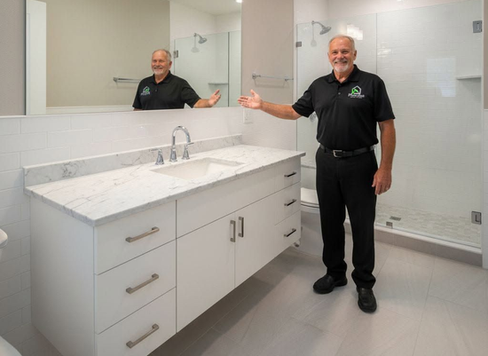 Man in black uniform standing in a bright modern bathroom with a double vanity and large mirror