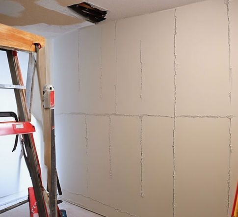 Partially plastered interior wall with patch lines, next to a ladder in a room under renovation