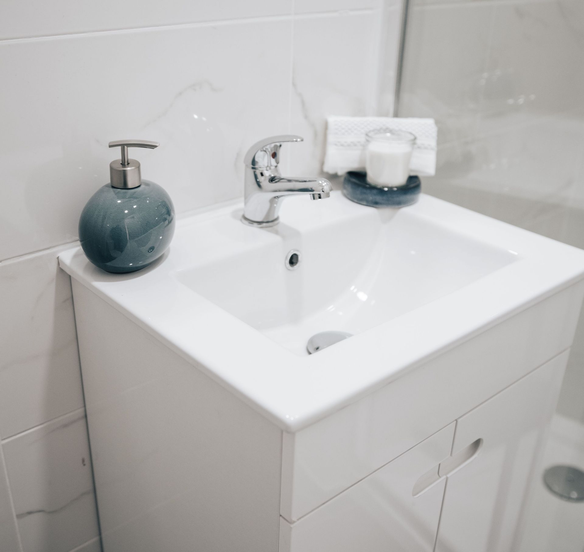 White bathroom sink with chrome faucet, soap dispensers, and a cabinet below