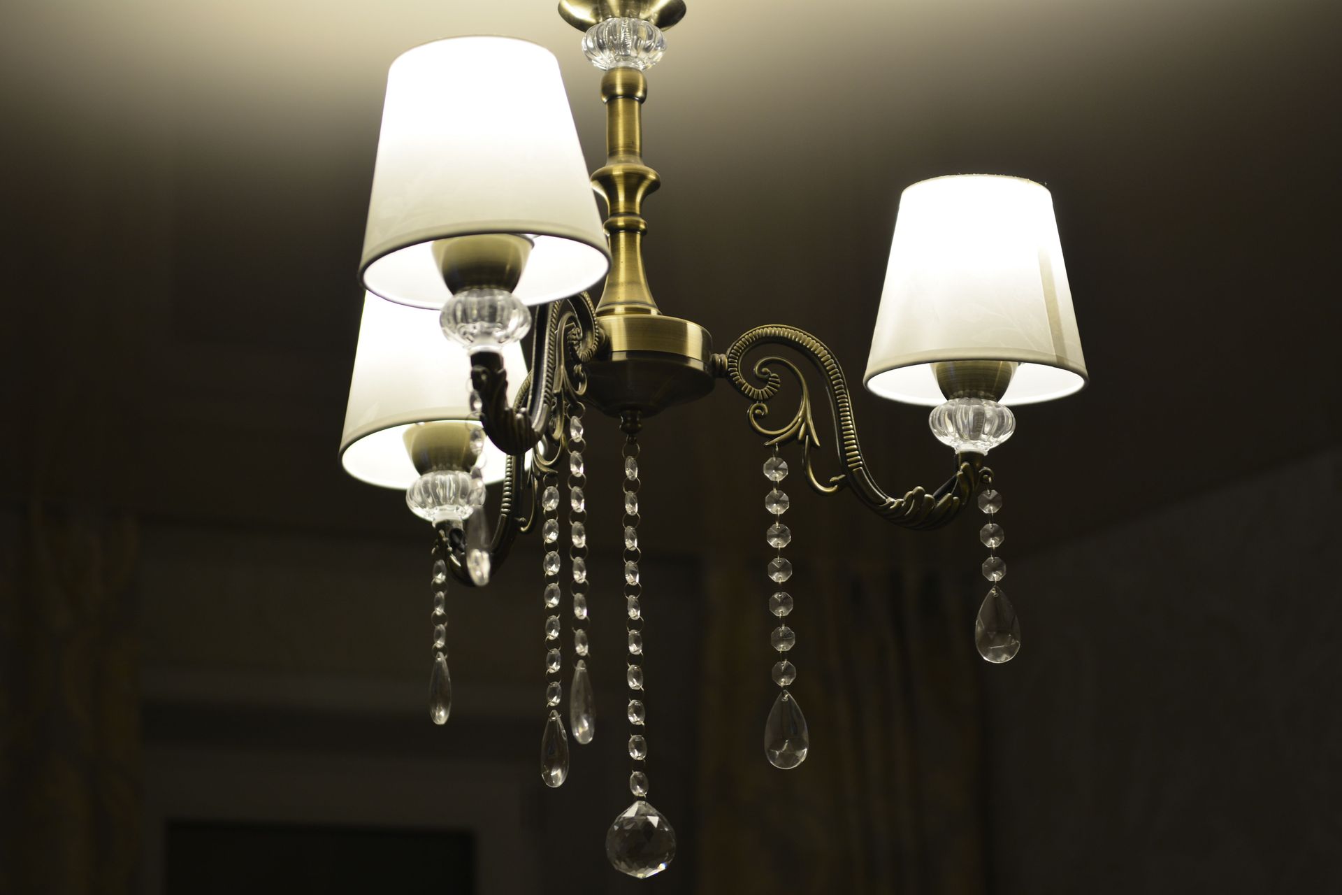 Chandelier with white lampshades and dangling crystal beads hanging from a ceiling