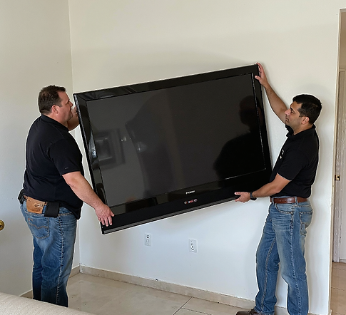 Two men carrying a large flat-screen TV through a room under construction