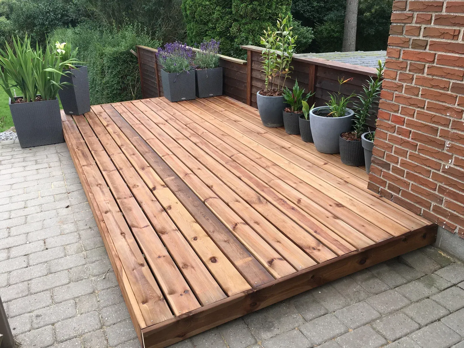 A wooden deck with potted plants on it next to a brick wall.