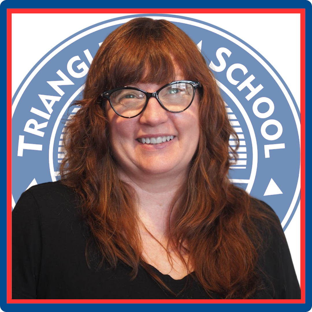 A woman wearing glasses is smiling in front of a triangl school logo