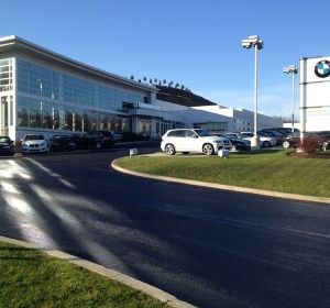 BMW dealership exterior with glass showroom, parked cars, and a curved driveway under a clear blue sky