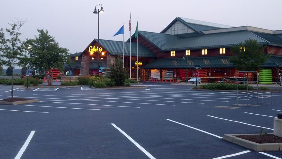 Empty parking lot outside a lit building at dusk with a flagpole and trees.