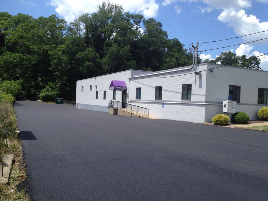 White building with purple awning beside an empty paved lot, backed by trees and power lines.