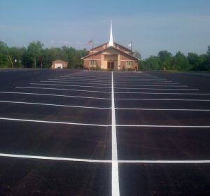 Empty blacktop parking lot leading to a small church with a white steeple
