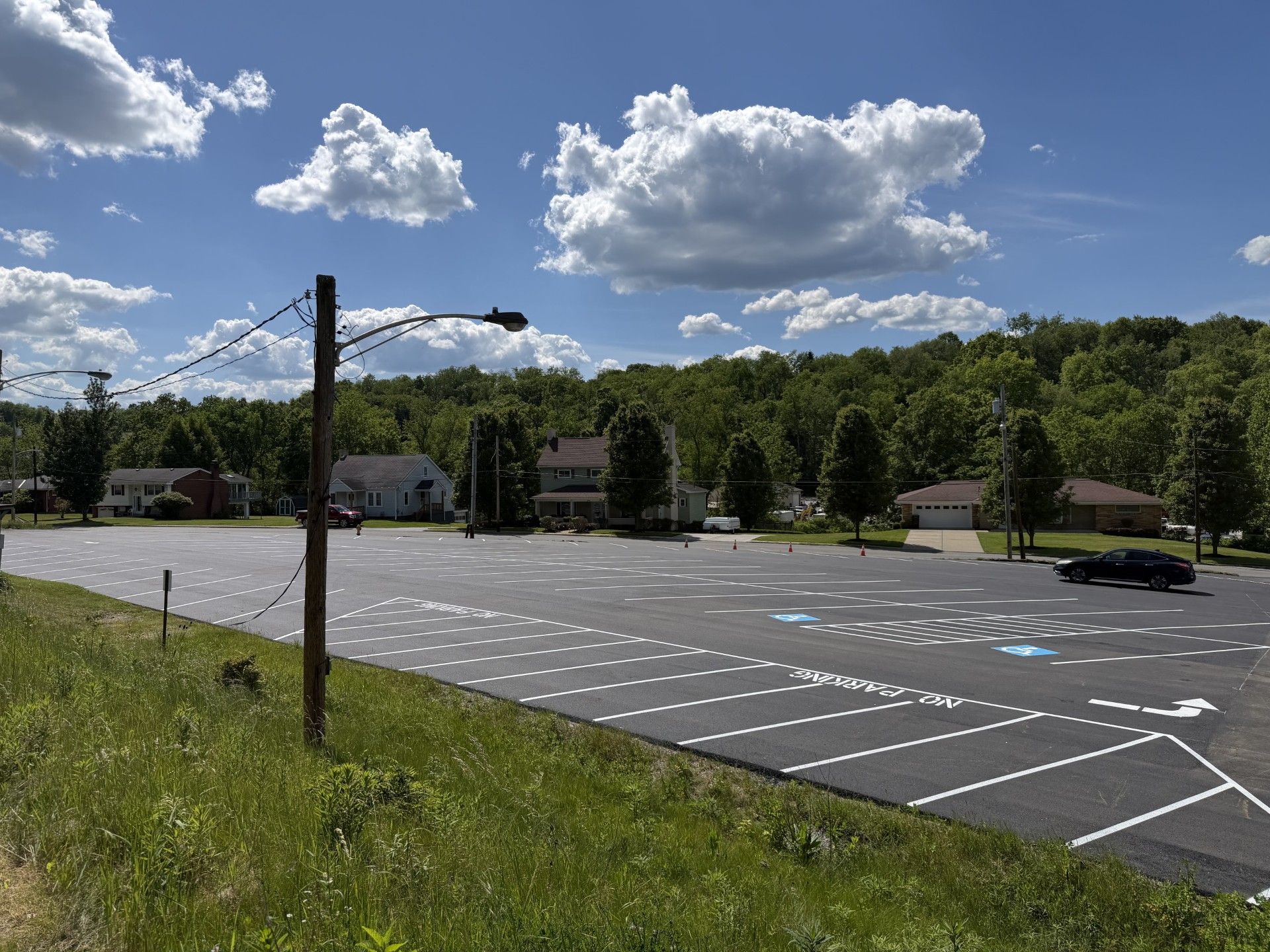 Empty parking lot by a wooded roadside under a blue sky with scattered clouds