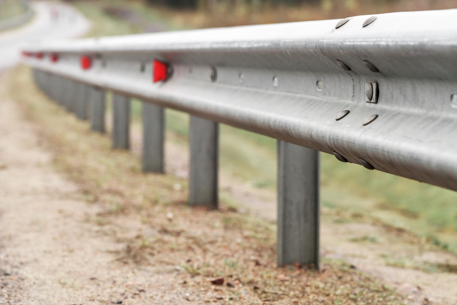 Close-up of a silver highway guardrail with red reflectors along a roadside