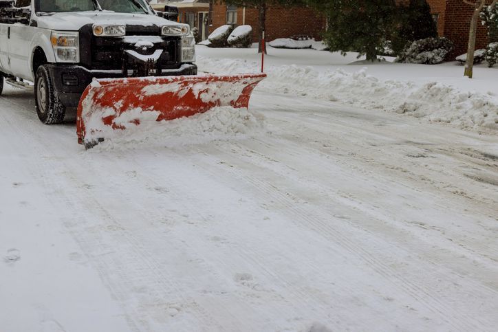 Snowplow clearing a snowy driveway with an orange plow blade attached to a black truck