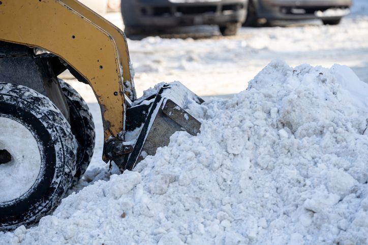 Yellow snowplow pushing snow in a snowy parking lot