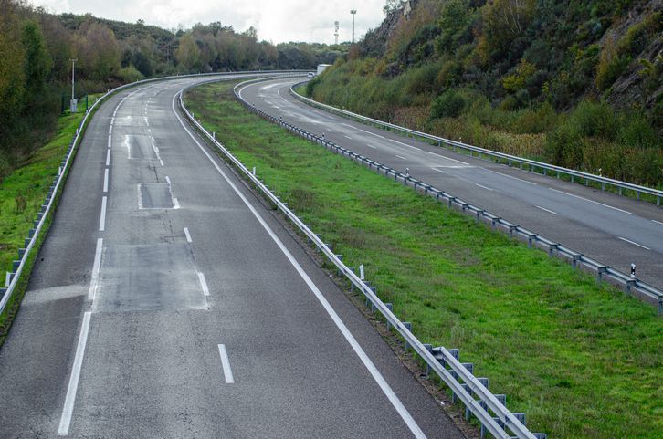 Empty multi-lane highway curving through green countryside under overcast skies