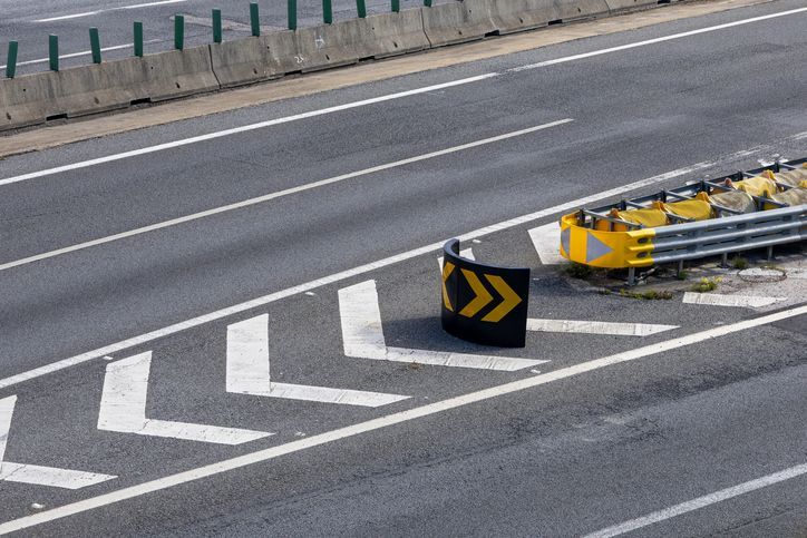 Curved highway barrier with black-and-yellow chevron sign and white road markings near a crash cushion