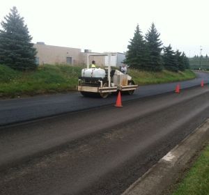 Road paving machine on a wet roadway with orange cones and evergreen trees nearby