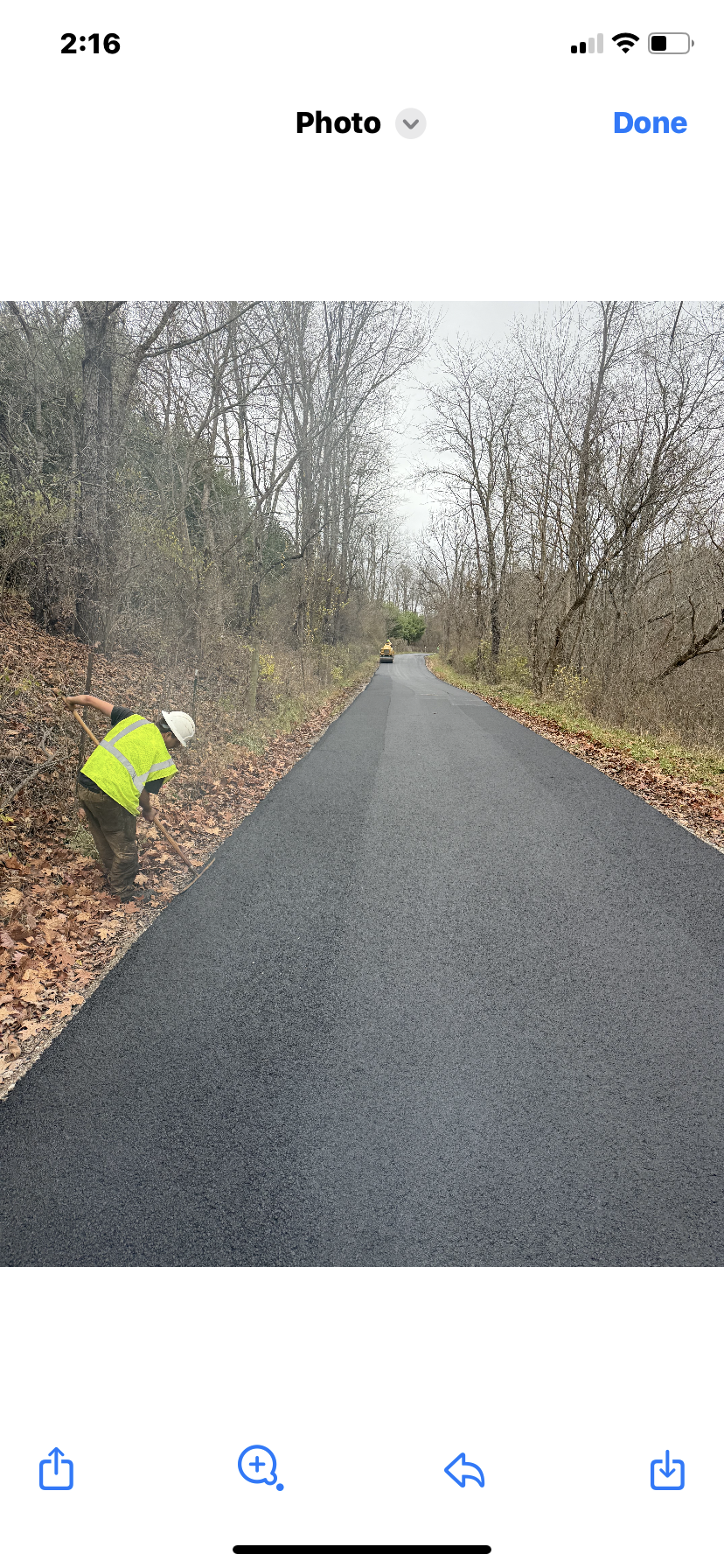 Person in a bright yellow jacket crouches beside a wet paved road in a wooded area.