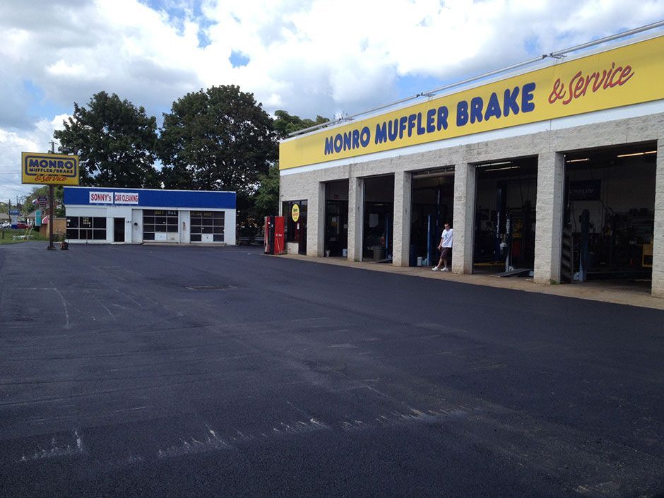 Auto repair shop with yellow sign and open service bays on a paved lot under a cloudy sky