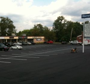 Large mostly empty parking lot with a few cars, storefronts in back, and a Sharper sign on the right.