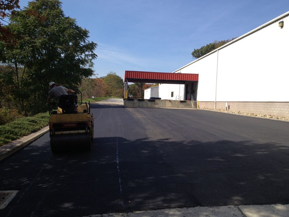 Road roller on a paved driveway beside a white building under a red canopy