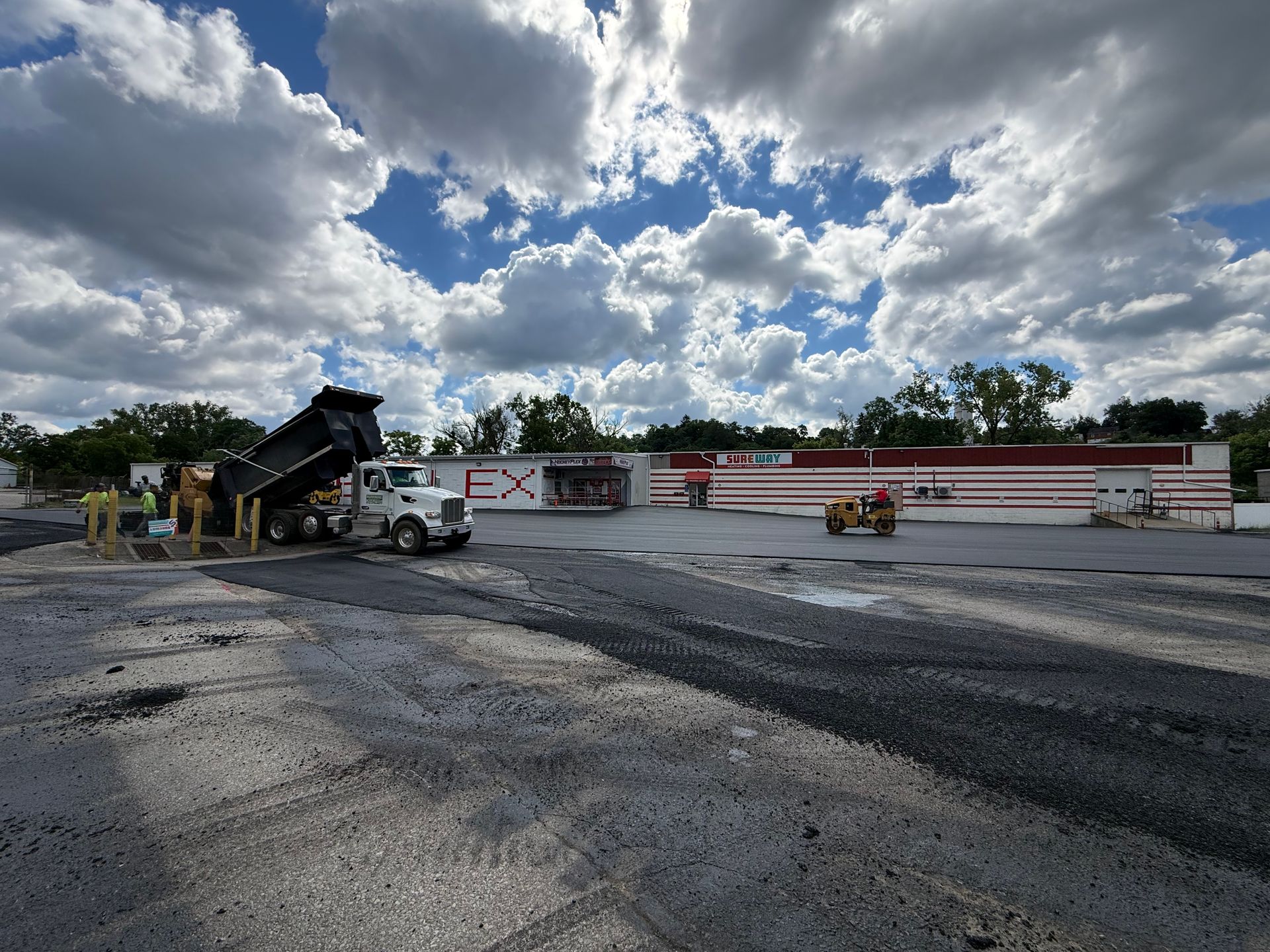 Damaged parking lot with cracked pavement, construction equipment, and a partly demolished building under cloudy skies
