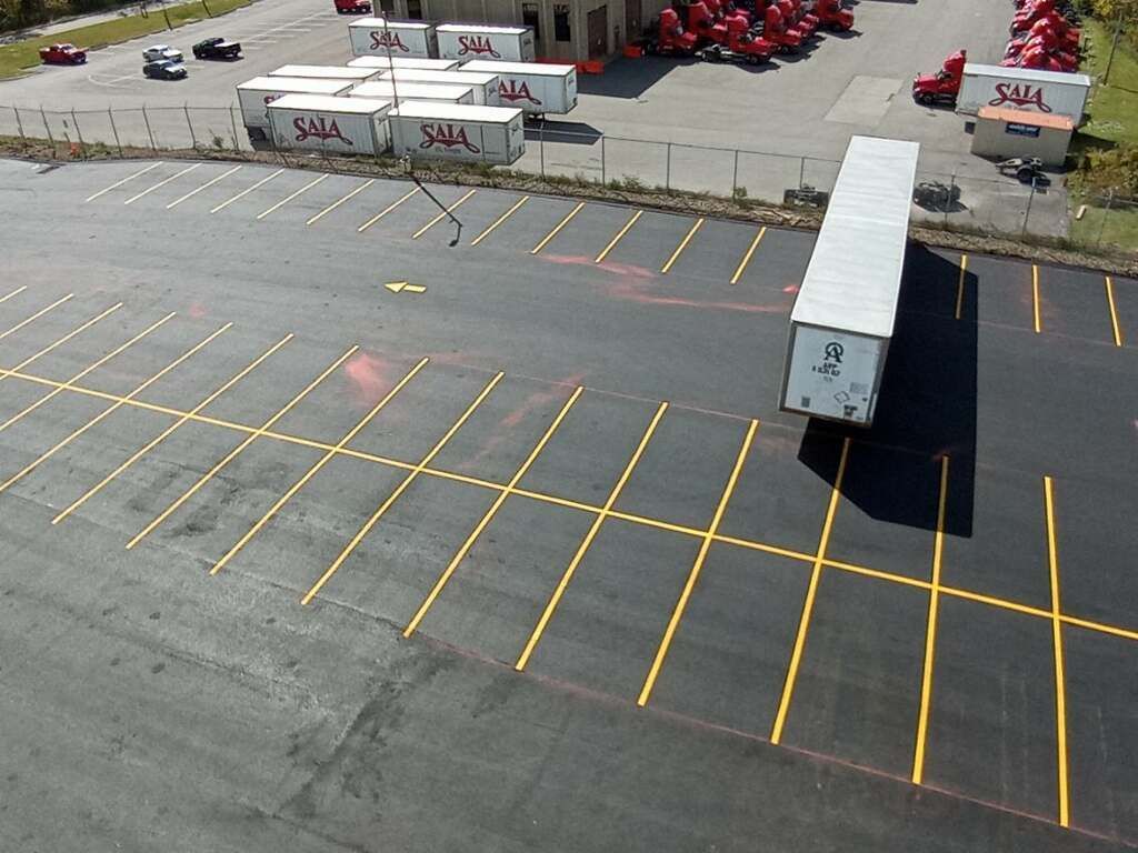 Empty parking lot beside several white semi-trailers and red trucks in a warehouse yard