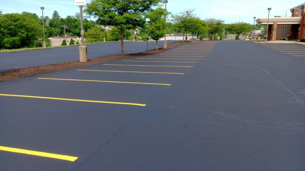 Empty parking lot with yellow lines beside a low wall and trees under a clear sky