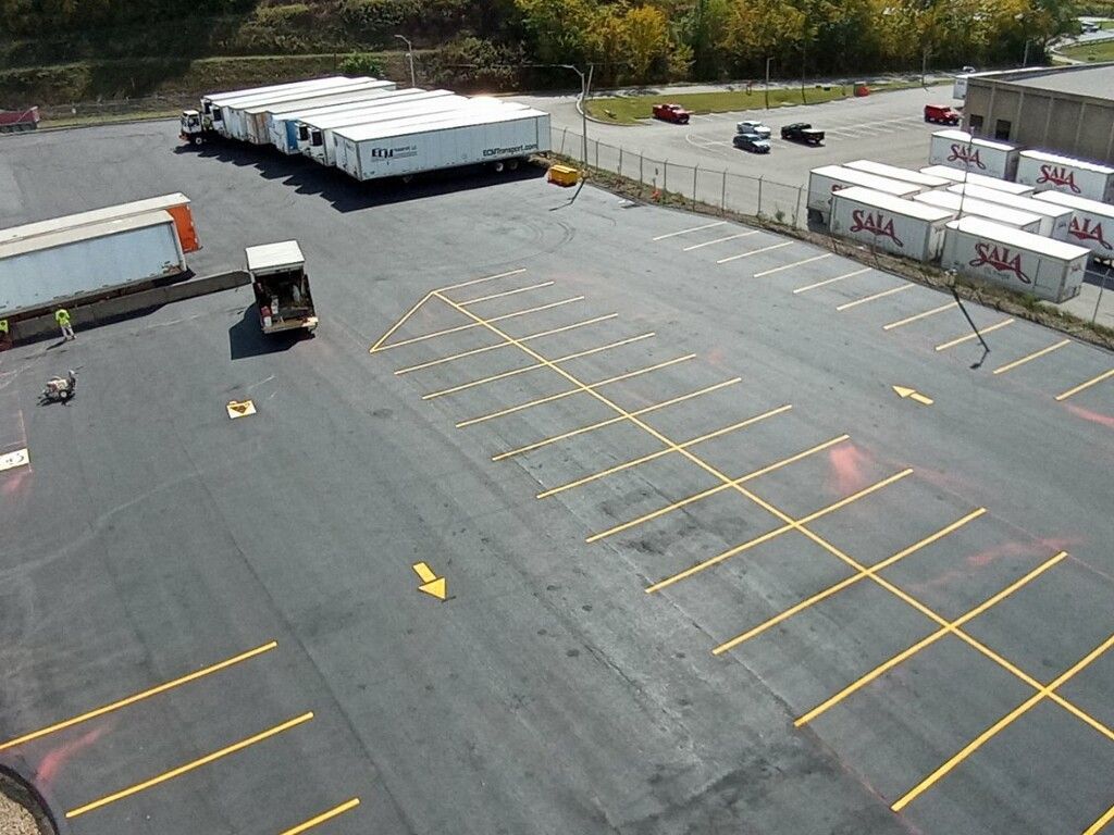 Empty parking lot with yellow spaces, a forklift, and parked trucks near a warehouse