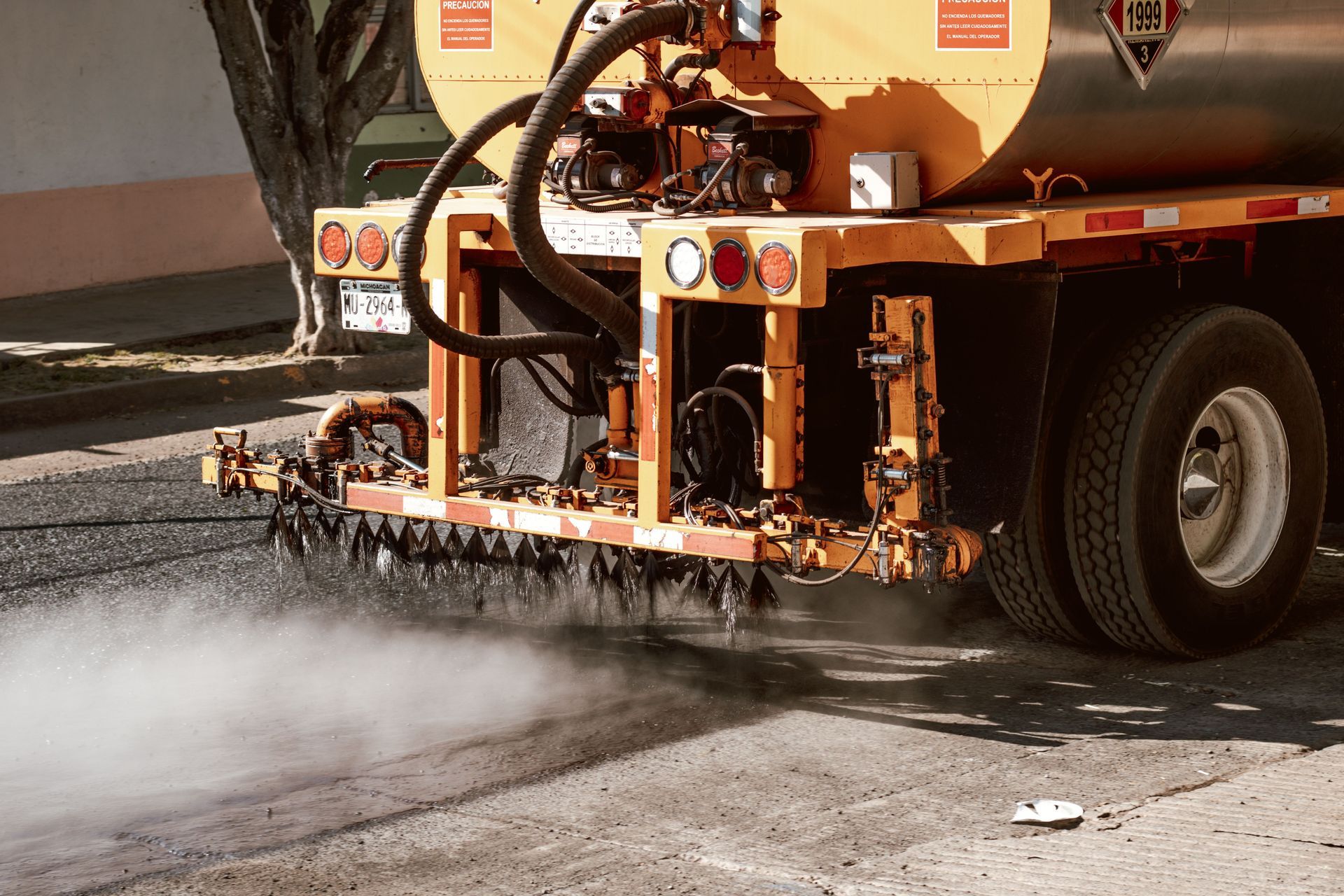 Street sweeper spraying water and brushing debris from pavement beside a truck wheel