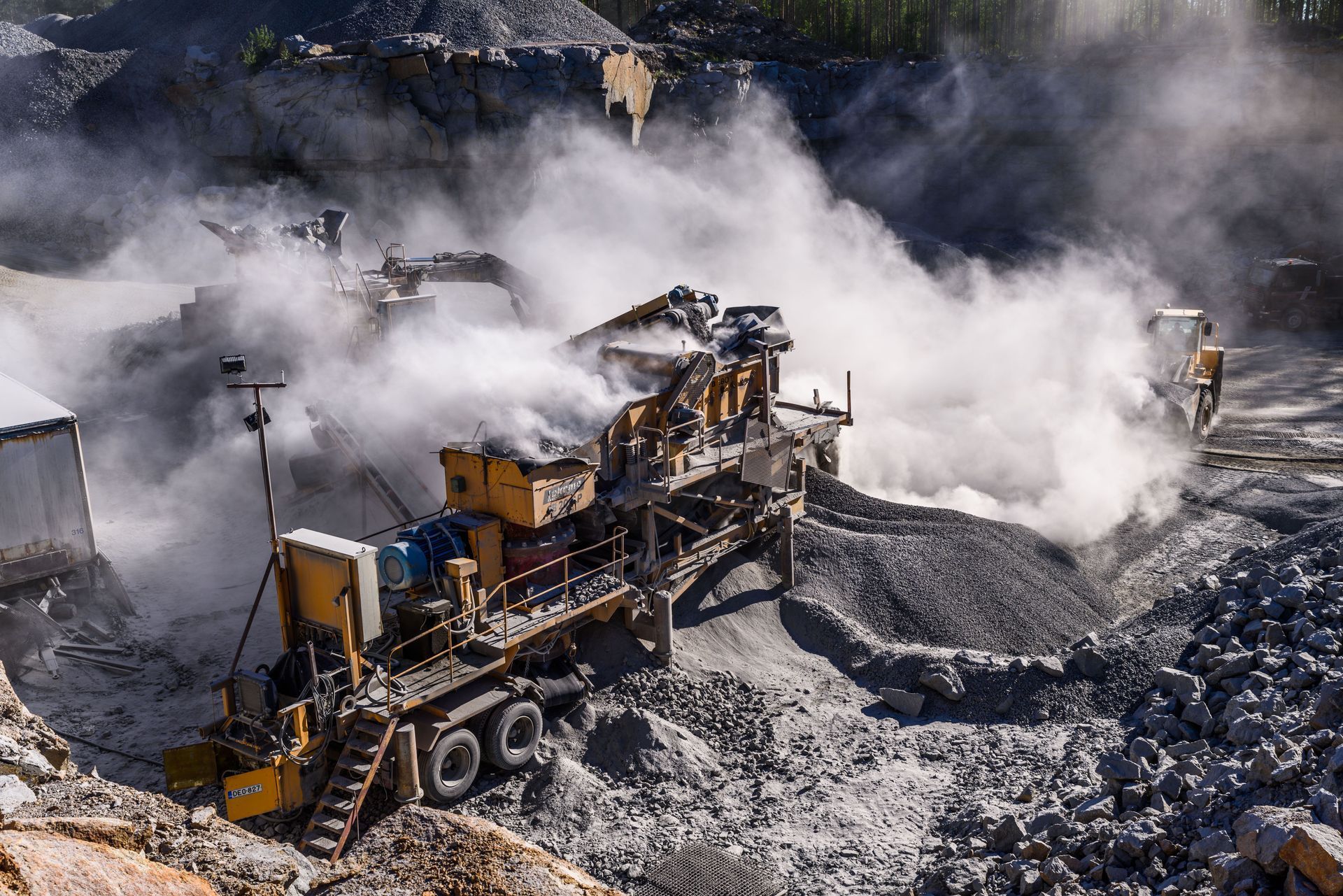 Heavy mining machinery excavates a rocky quarry, kicking up dust and smoke.