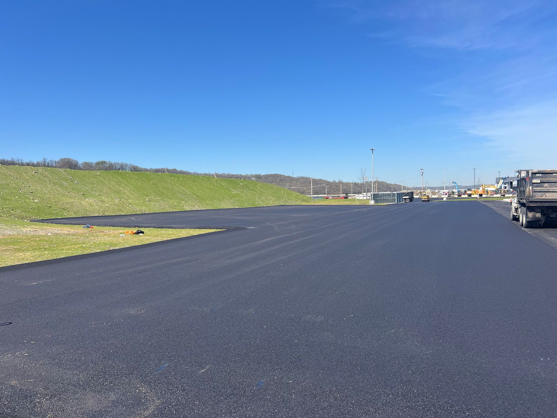 Freshly paved road beside a grassy embankment under a bright blue sky